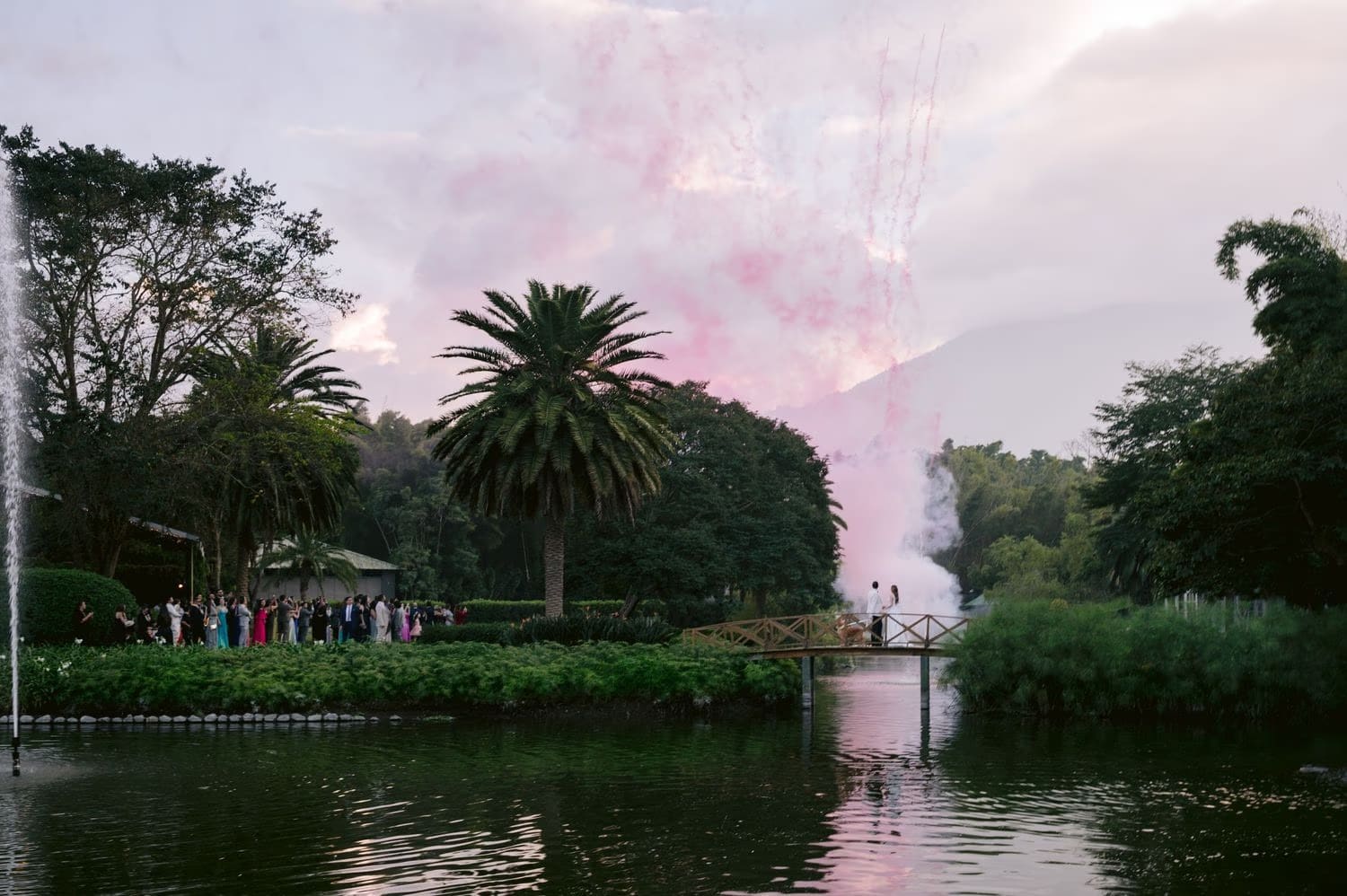 Pink fireworks erupt over the bridge while guests watch from the lagoon edge at Villa Bokeh.