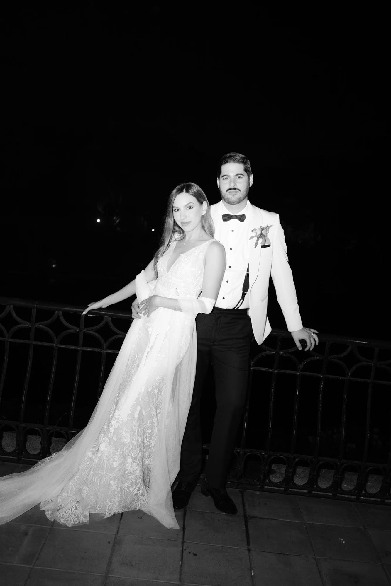 Bride and groom lean on a terrace railing at night in black and white — second look at Villa Bokeh.