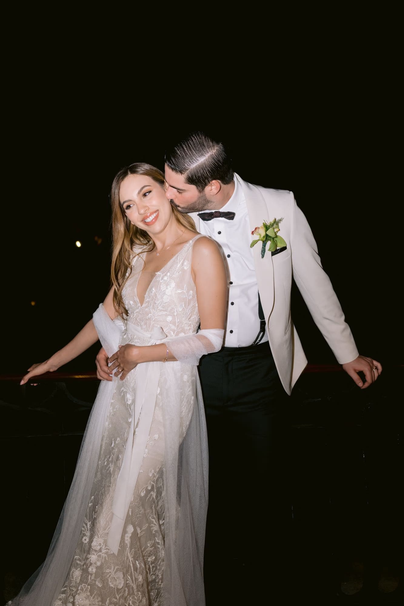 Sergio kisses Caro's temple at night, her embroidered second-look gown glowing — Villa Bokeh wedding.