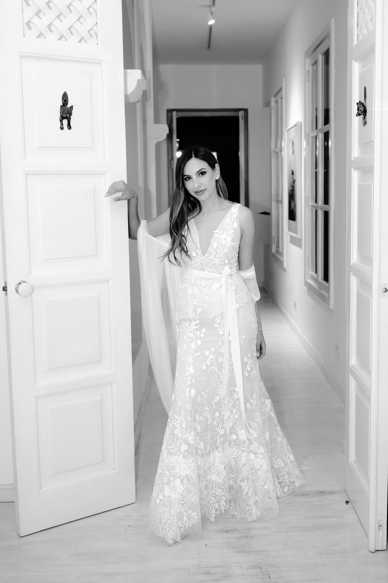 Black-and-white portrait of Caro in her embroidered second-look gown in a colonial hallway.