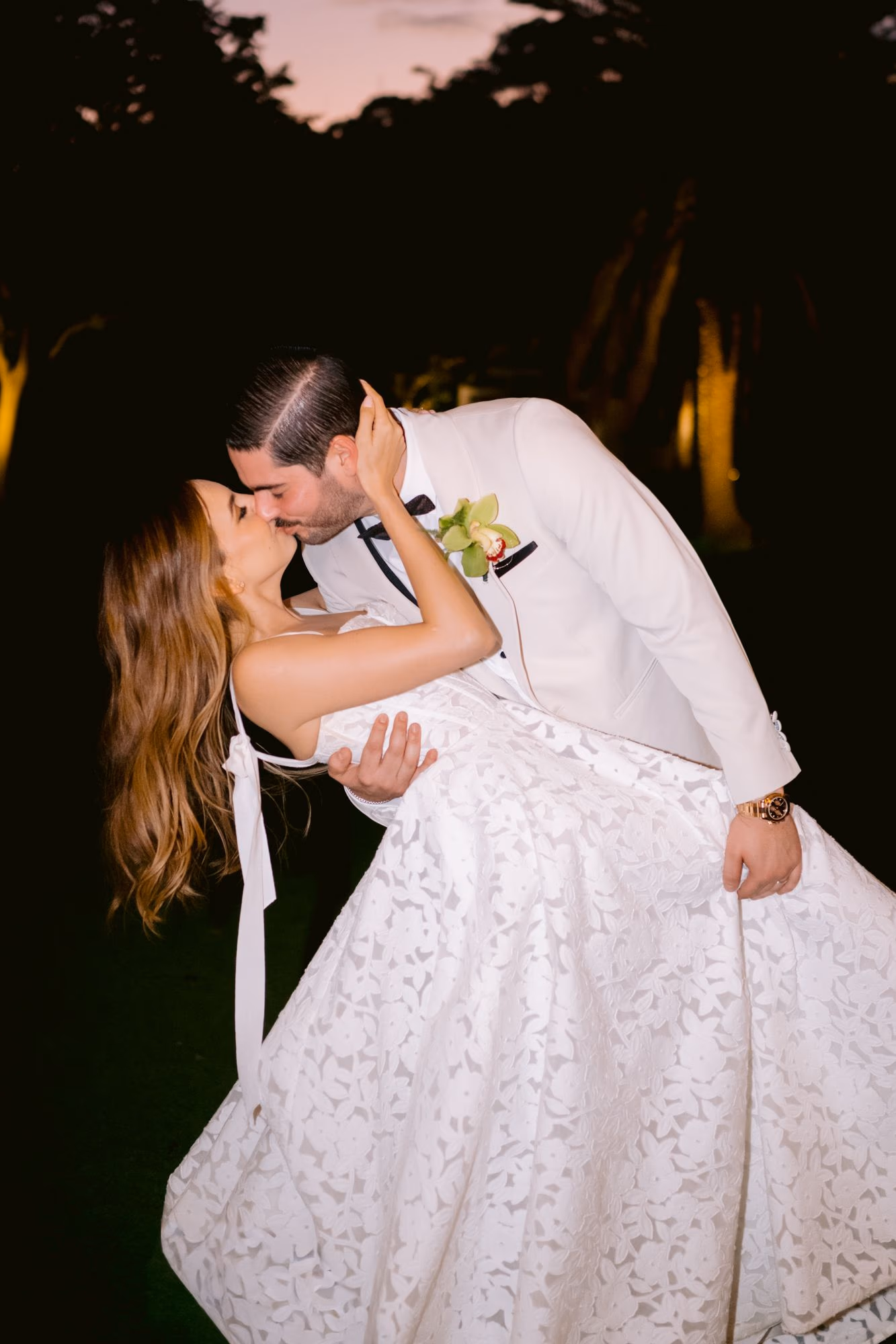 Groom dips Caro into a kiss under twilight trees in the gardens of Villa Bokeh, Antigua Guatemala — editorial destination wedding portrait at dusk.