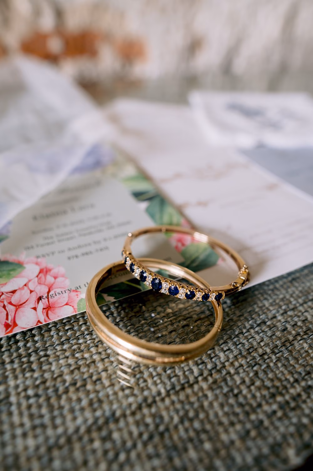 Gold wedding bands with sapphire and diamond eternity ring resting on watercolor invitation — bridal jewelry detail.