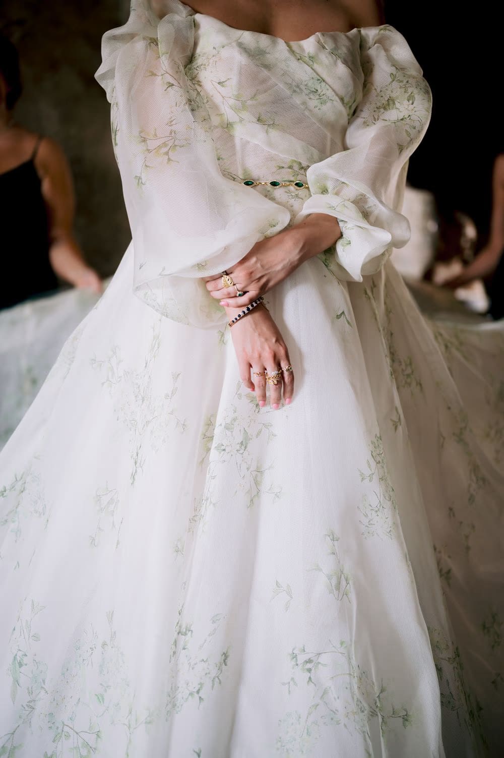 Detail of the bride's floral-embroidered organza gown with emerald belt and stacked rings during getting-ready.