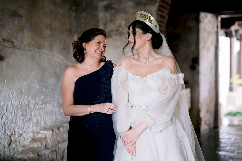 Mother of the bride smiles at her daughter inside a stone passageway before the ceremony — intimate getting-ready portrait.