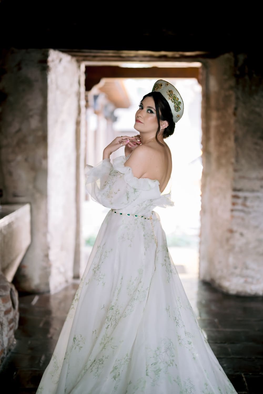 Bride looks over her shoulder in floral gown inside a sunlit colonnade of the restored monastery.