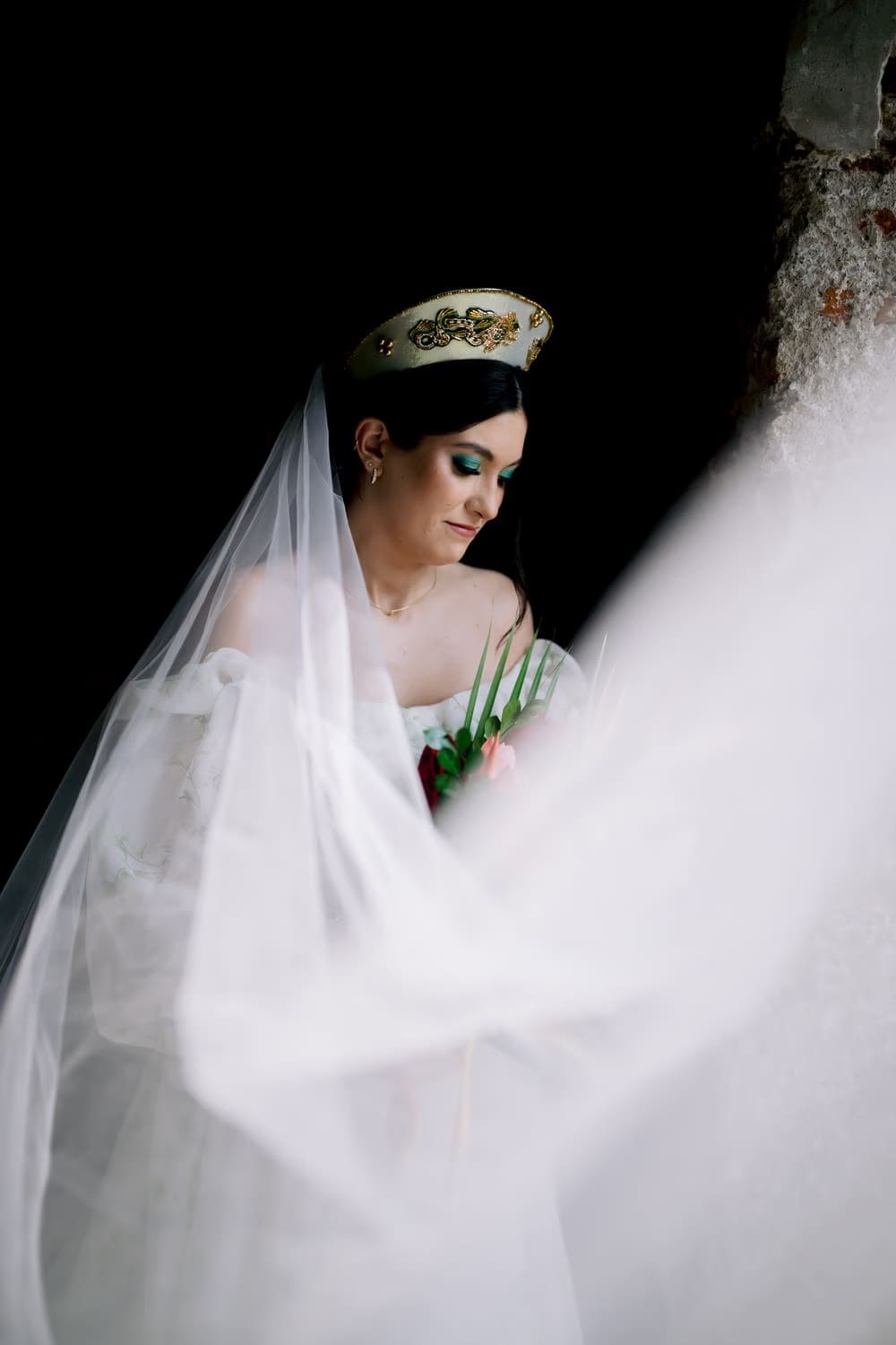 Bride in soft profile with veil flowing across the frame against a black backdrop — dramatic editorial portrait.
