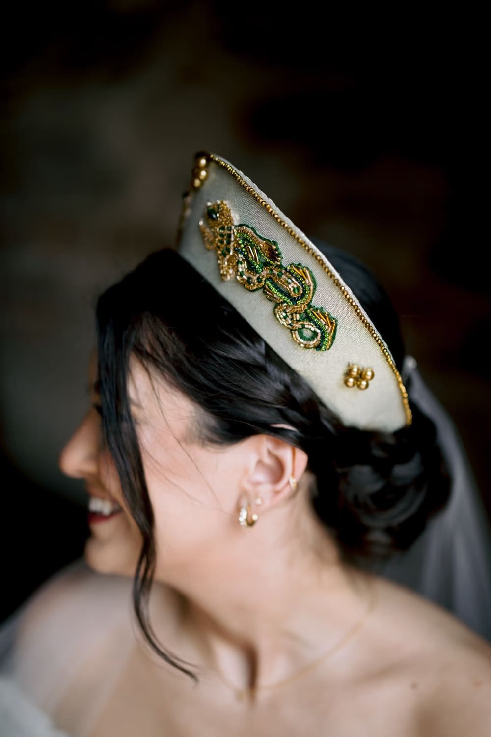 Close-up of beaded green-and-gold bridal crown with bare shoulder and gold drop earring — accessory detail.