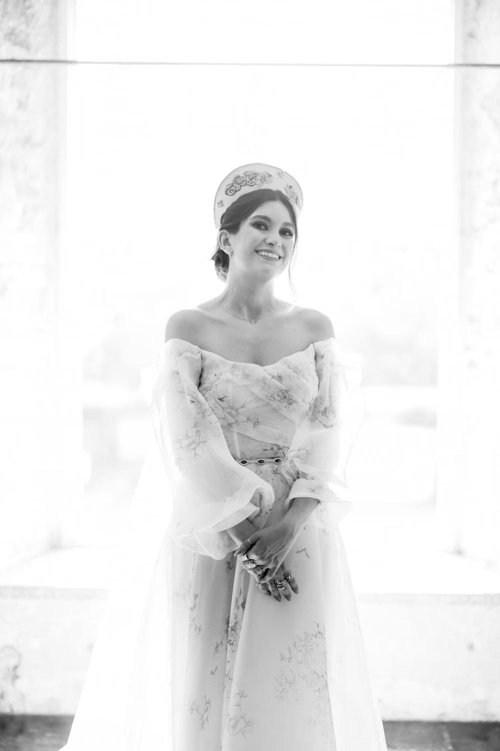 Backlit black-and-white bridal portrait inside a tall arched window — soft editorial frame.