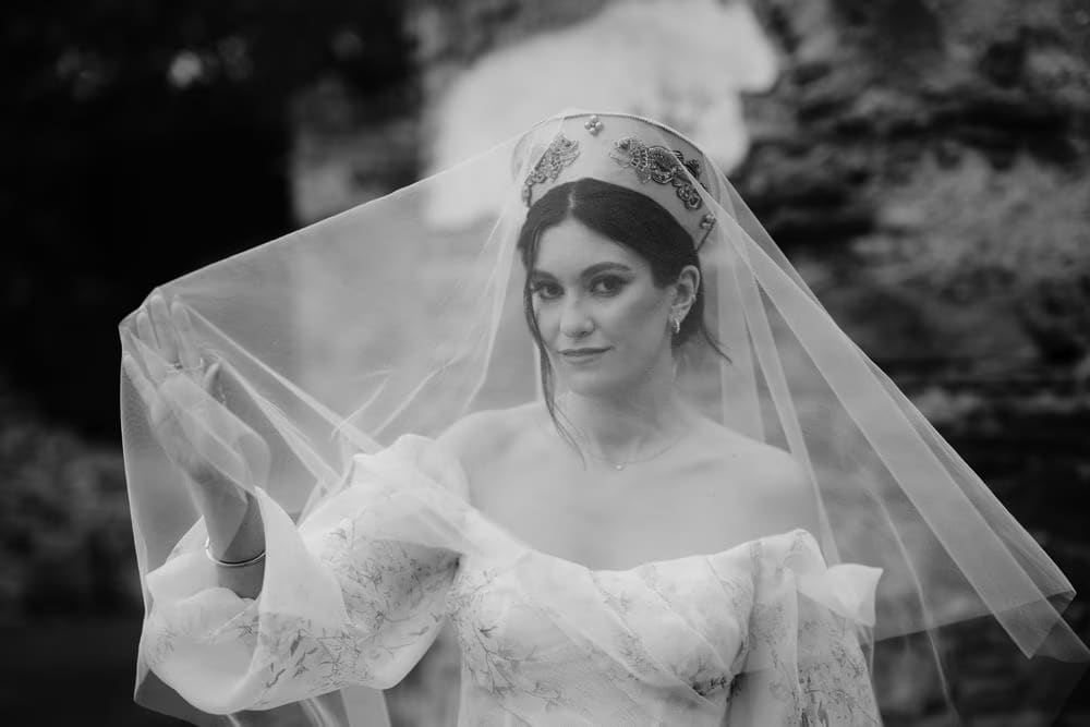 Black-and-white close-up of the bride peering through her veil with beaded crown and dramatic eye makeup.