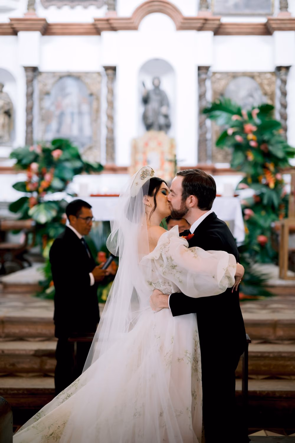 Bride and groom share their first kiss in front of the baroque altar and tropical floral arch.