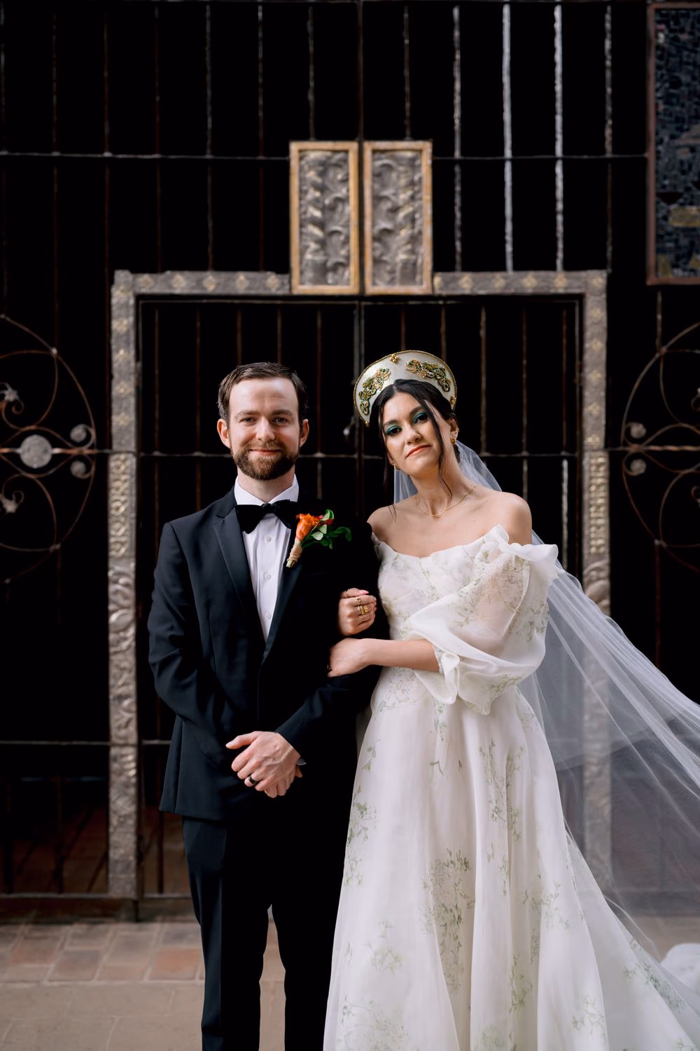 Newlyweds pose arm-in-arm in front of a hand-carved metal gate at Hotel Casa Santo Domingo — formal couple portrait.