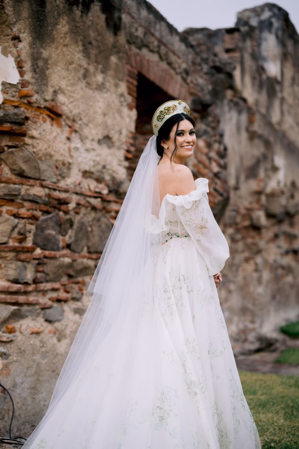Bride glances over her shoulder among brick monastery ruins, veil cascading down her back.