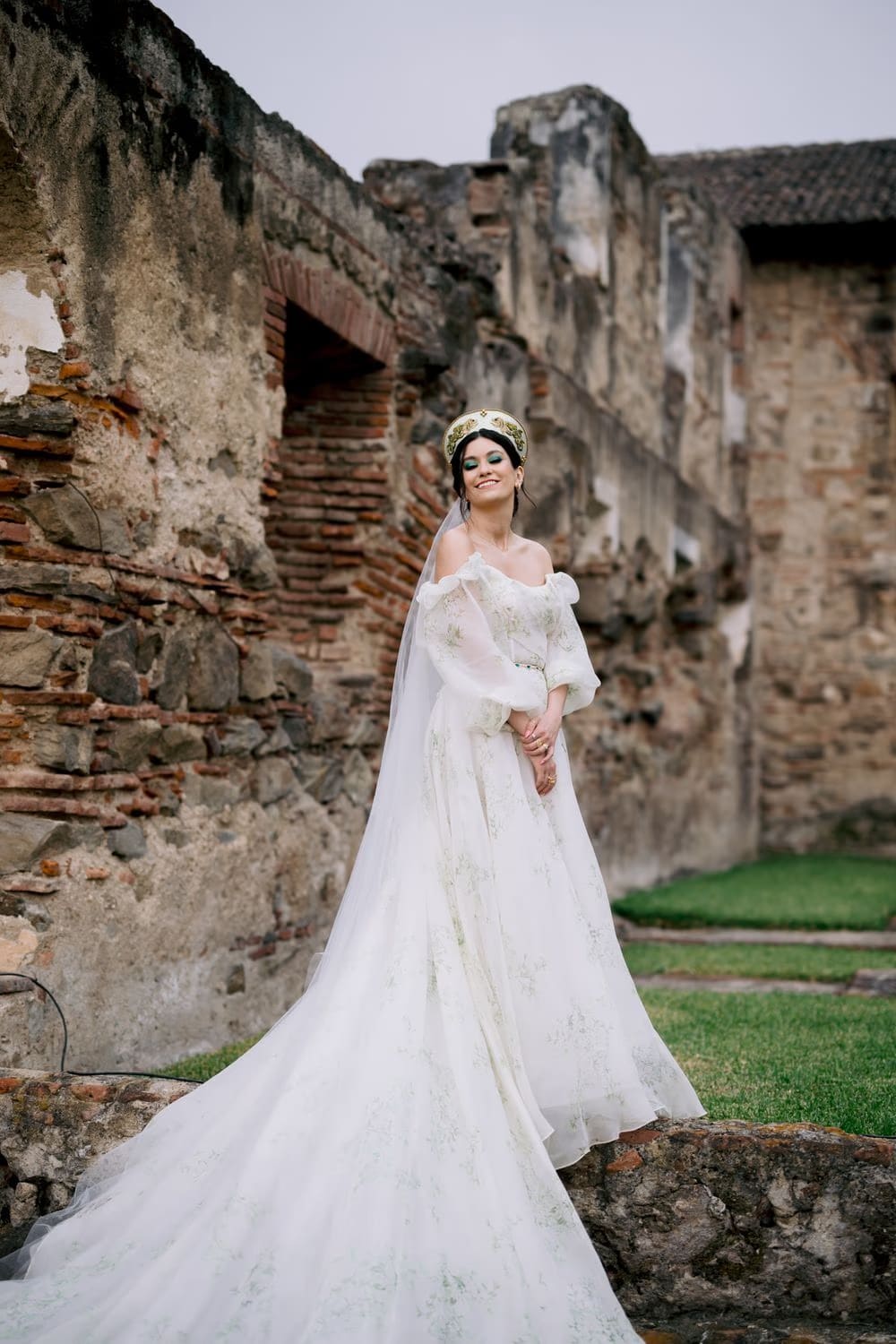 Bride poses on a stone ledge among brick ruins at Casa Santo Domingo — full-length destination bridal portrait in Antigua Guatemala.