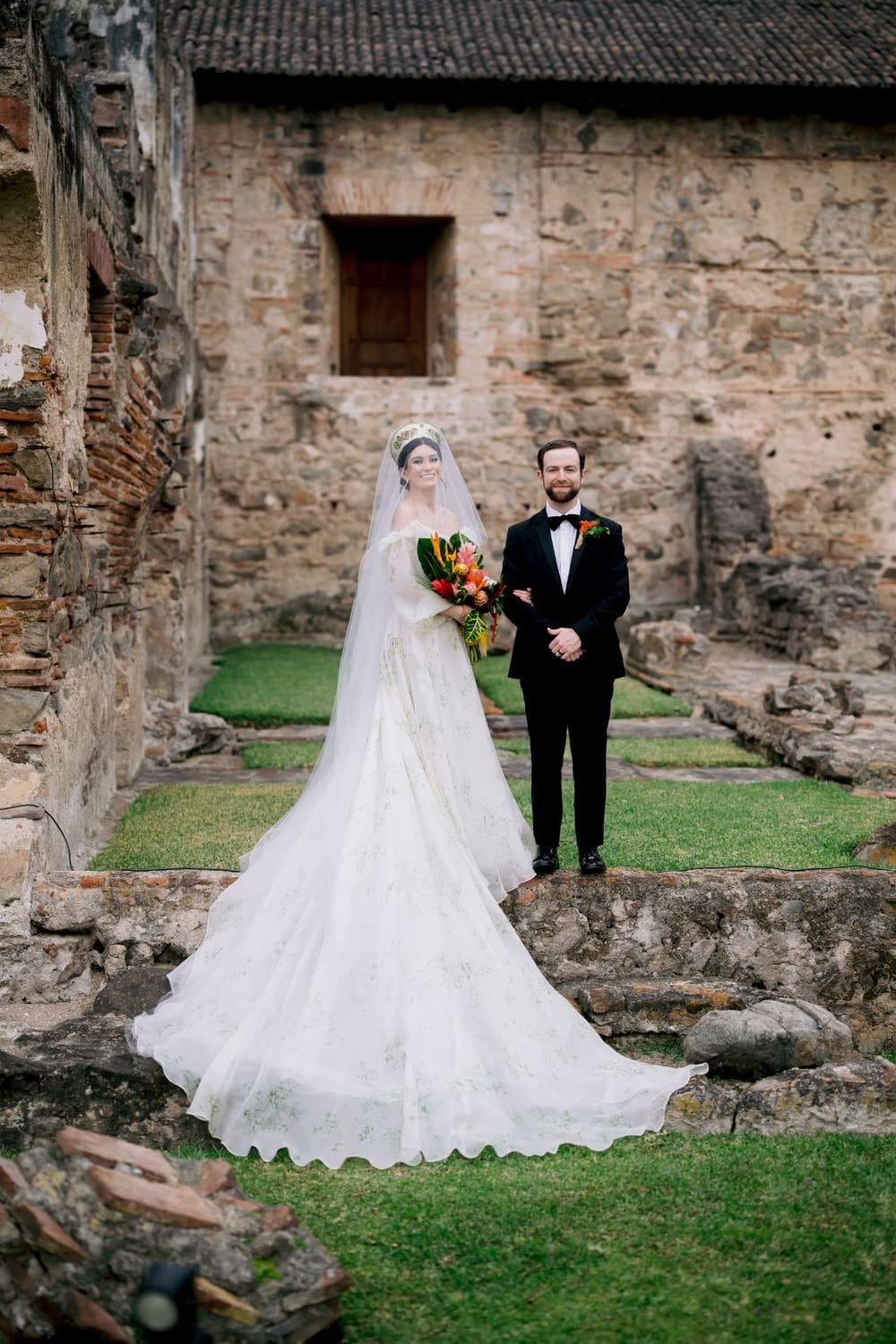 Newlyweds stand among the open monastery ruins, bride holding tropical bouquet — destination wedding portrait at Hotel Casa Santo Domingo.