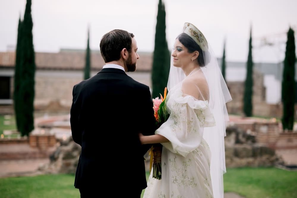Couple share a tender look between cypress trees in the monastery garden after the ceremony.
