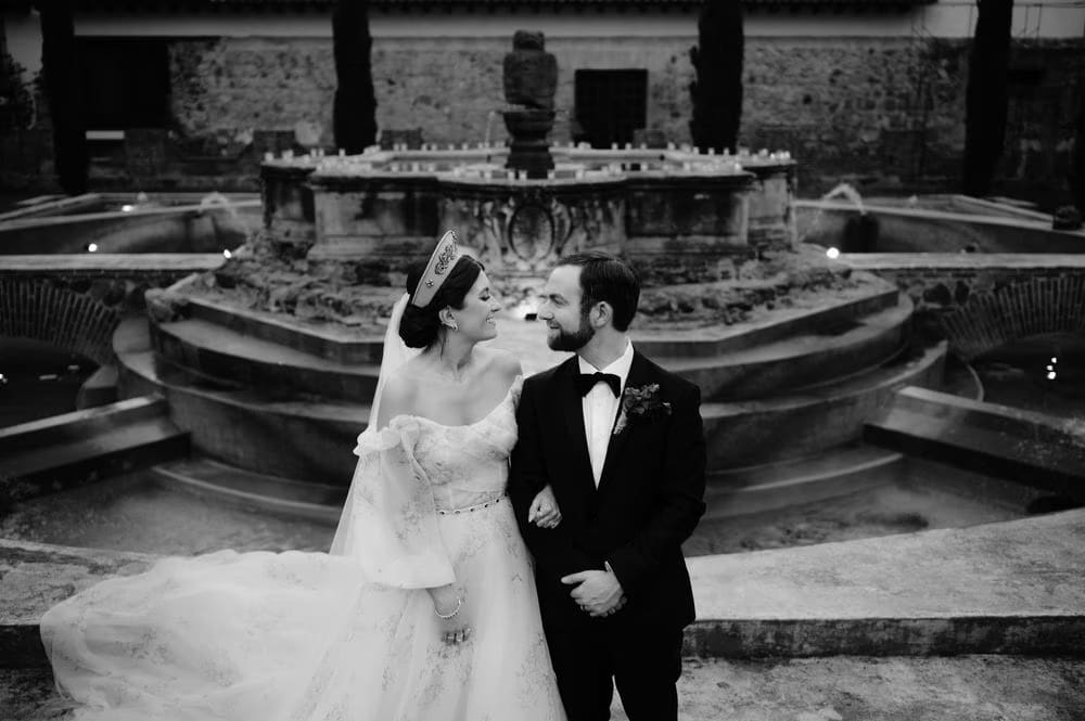 Black-and-white portrait of the newlyweds laughing arm-in-arm in front of the lit central fountain.