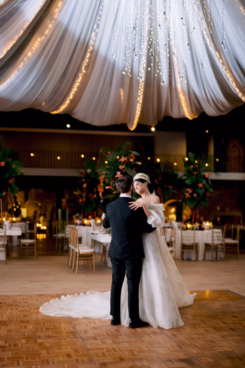 Elaina and Matt share their first dance beneath a draped fairy-light canopy at the Casa Santo Domingo reception, Antigua Guatemala — planning by Saguzo Eventos.