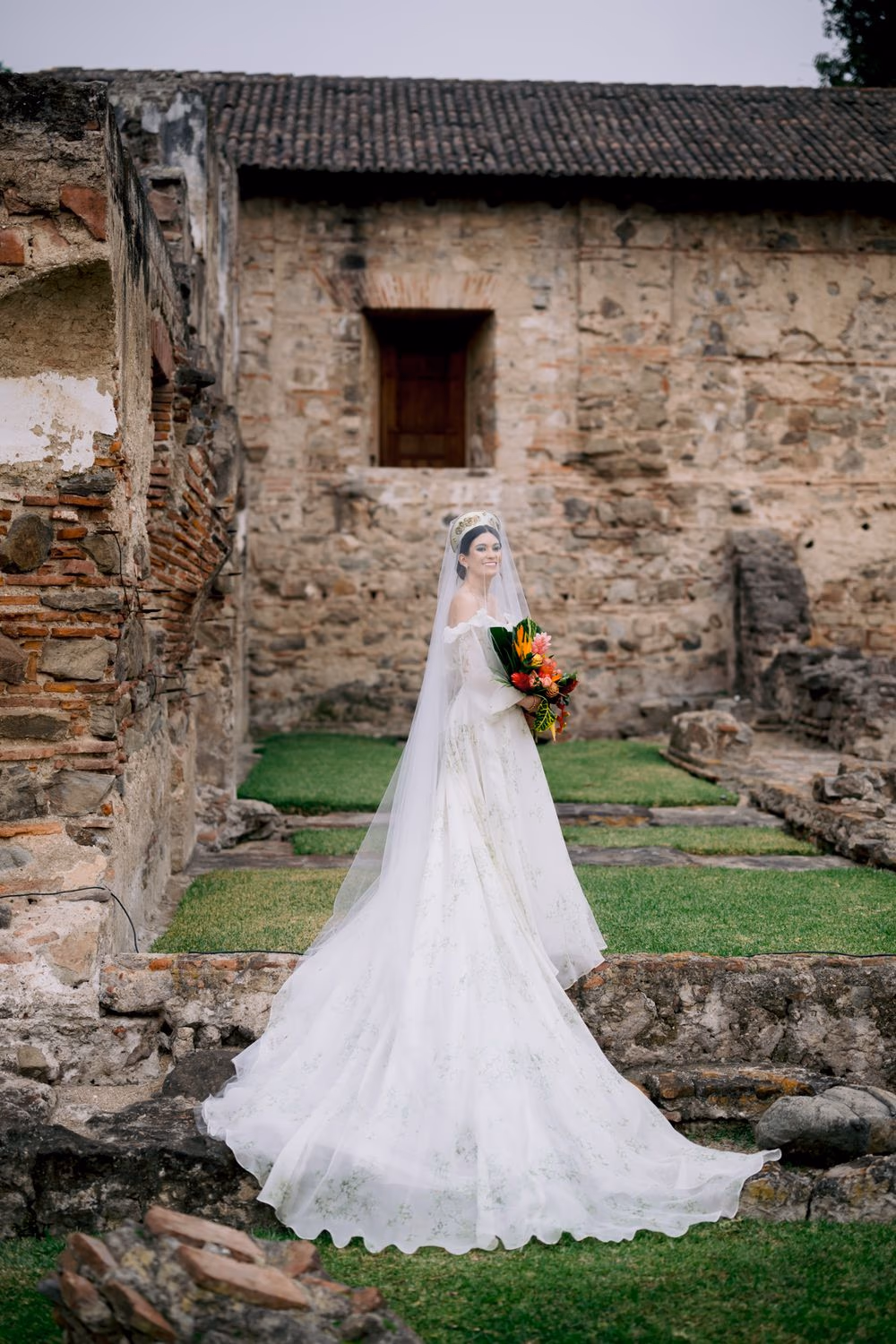 Bride Elaina poses with tropical bouquet in front of stone monastery ruins at Hotel Casa Santo Domingo, Antigua Guatemala — editorial wedding portrait inside restored monastery courtyard.