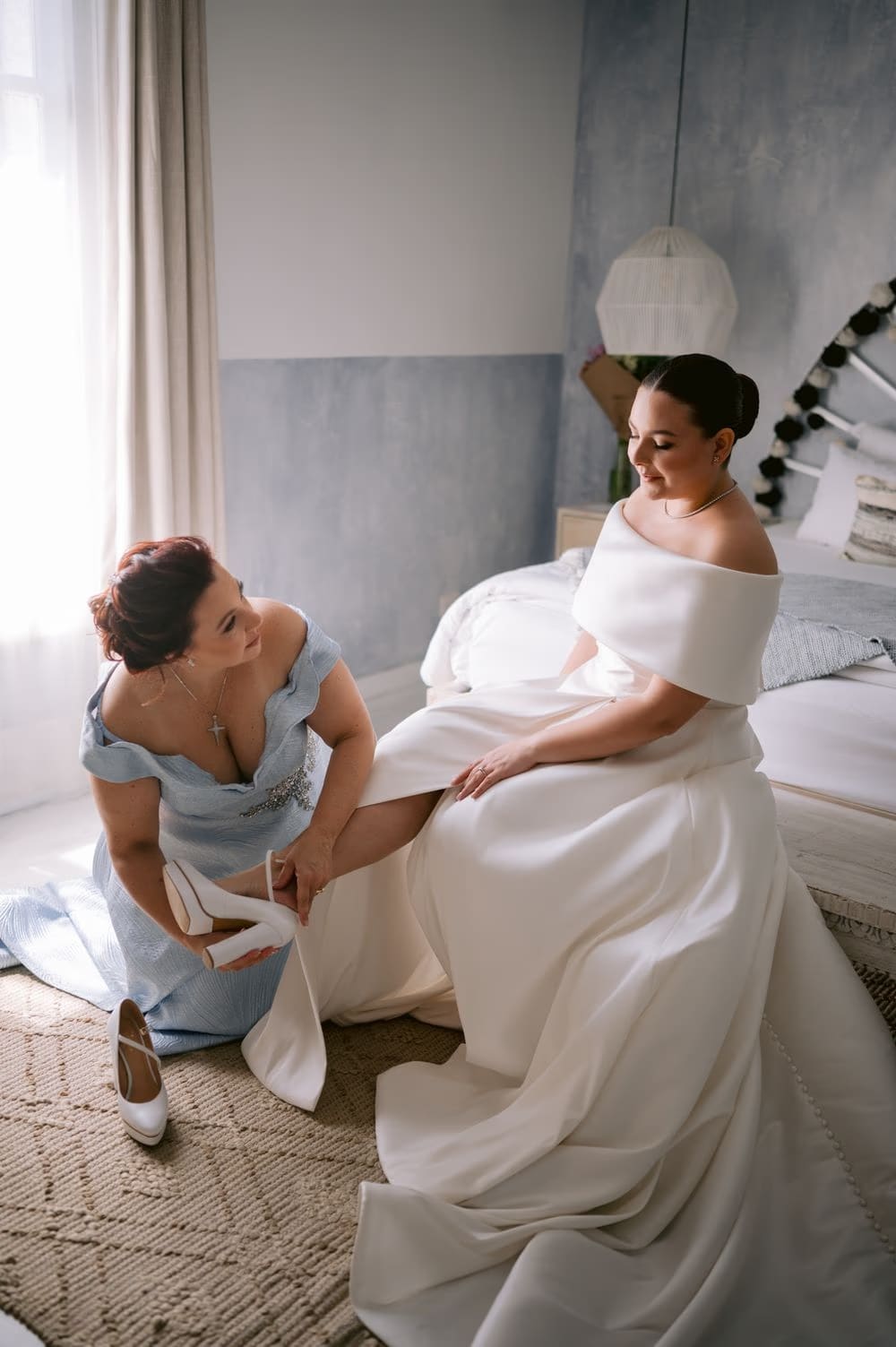 A bridesmaid in pale-blue helps Johanna with her wedding shoes during getting ready at Villa Bokeh.