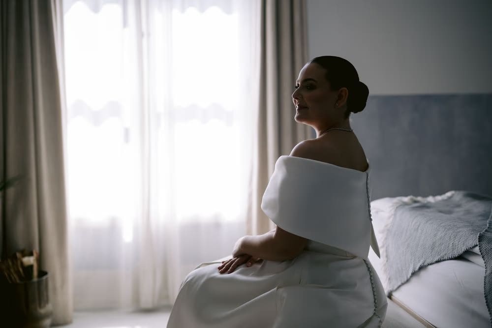Bride Johanna in soft window light wearing her structured off-shoulder gown during the morning of the wedding.