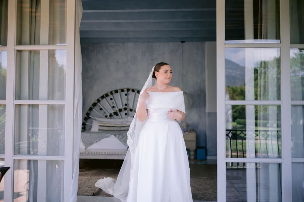 Bride poised in a French-door archway at the villa with her veil cascading behind her — modern bridal portrait.