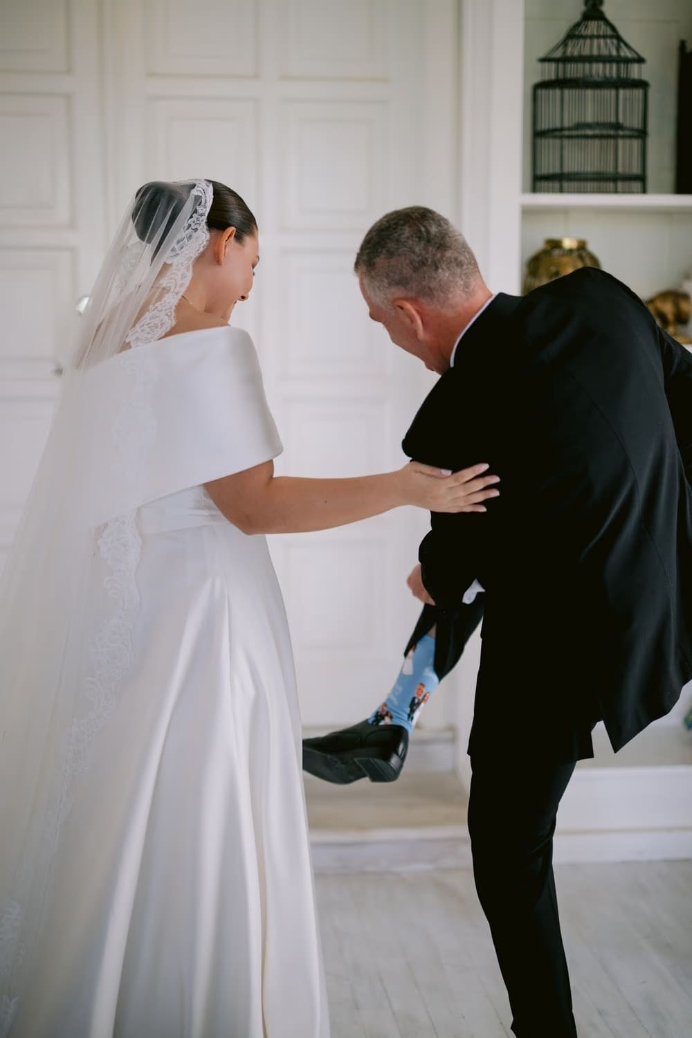 The father lifts his trouser to reveal custom socks printed with photos of the bride — playful first-look moment.
