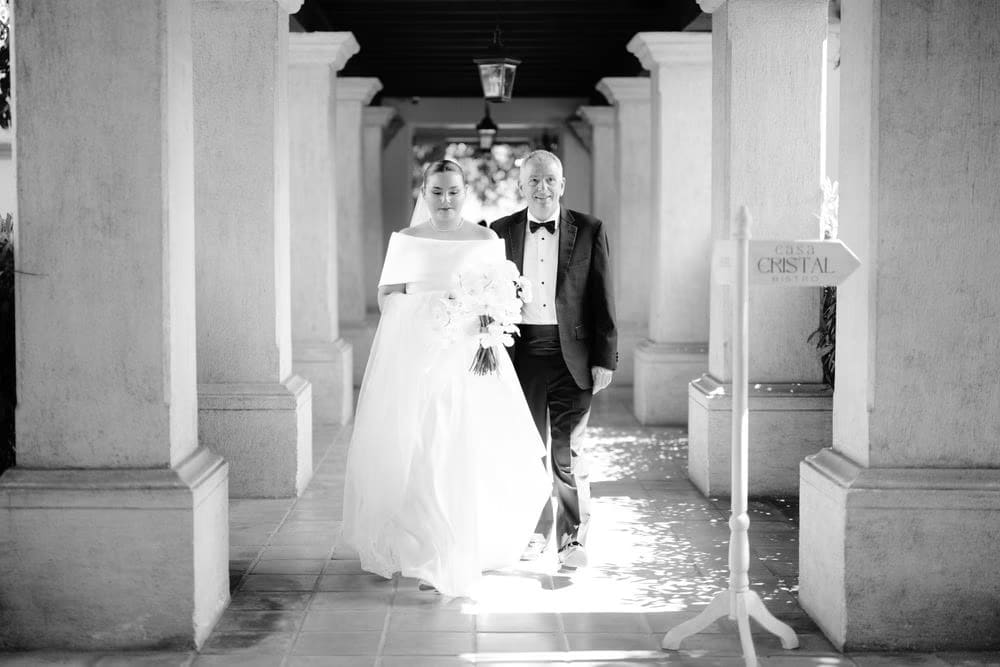 Bride and father walk through a colonnaded corridor in colonial Antigua on the way to the church.