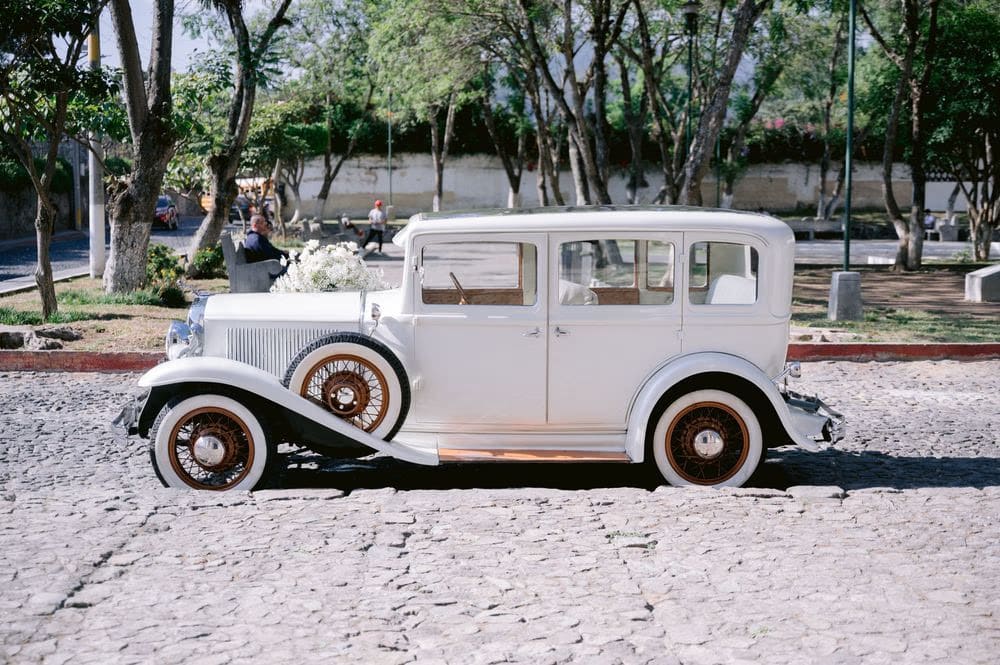 The vintage white wedding car parked on a cobbled street with a baby's breath bouquet on the hood — Antigua Guatemala.