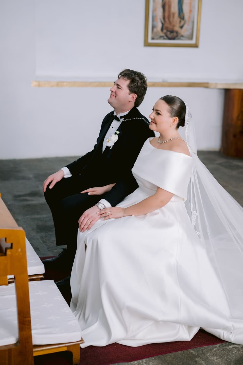 Bride and groom seated together at the ceremony beneath an image of the Virgin of Guadalupe.