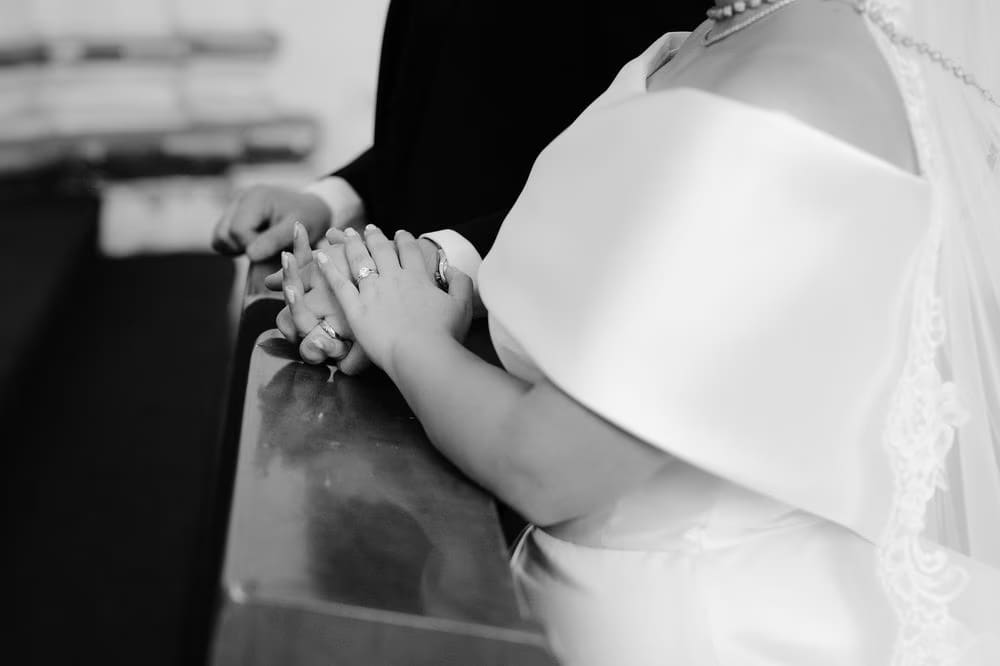 Black-and-white detail of the couple's hands resting together during the ceremony — wedding rings exchanged.