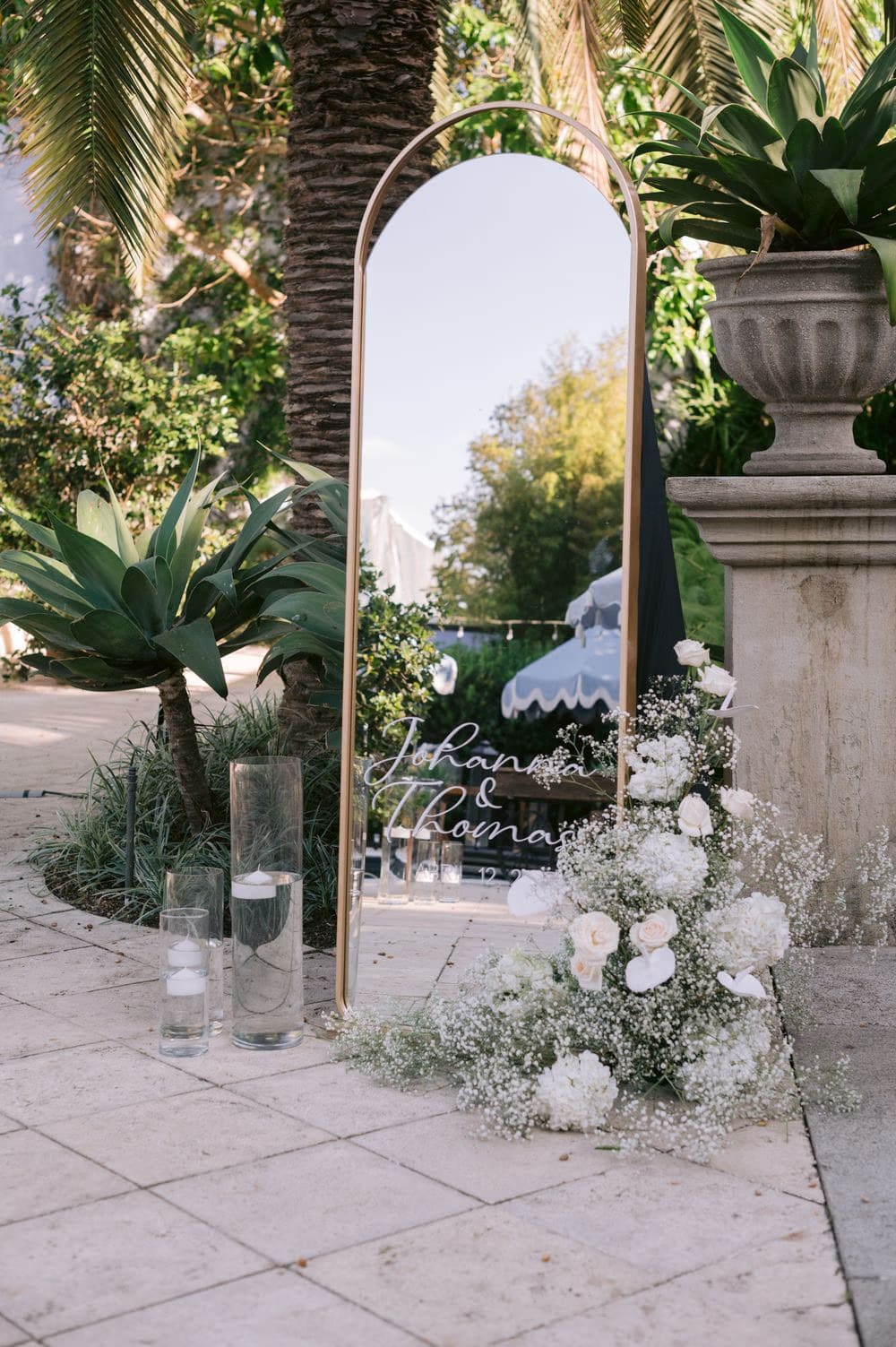 Gold arch mirror welcome sign hand-lettered with Johanna and Thomas, dressed with white roses and baby's breath by Decor Guatemala.