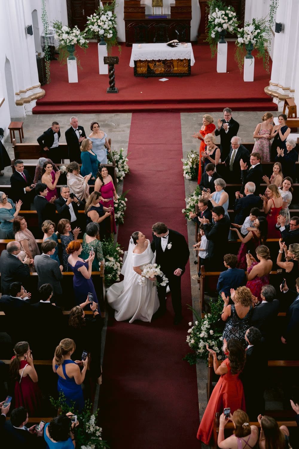Aerial view of the newlyweds walking back up the aisle with white florals along their path.