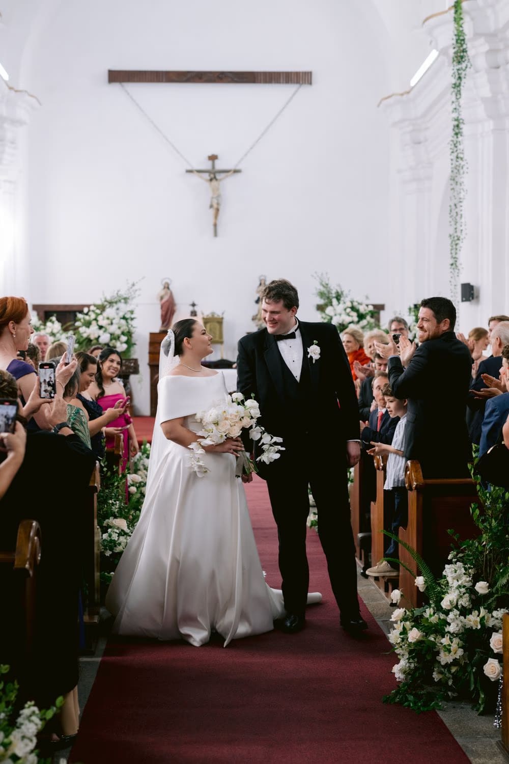 Bride and groom laugh during the recessional, surrounded by clapping guests — colonial church in Antigua.