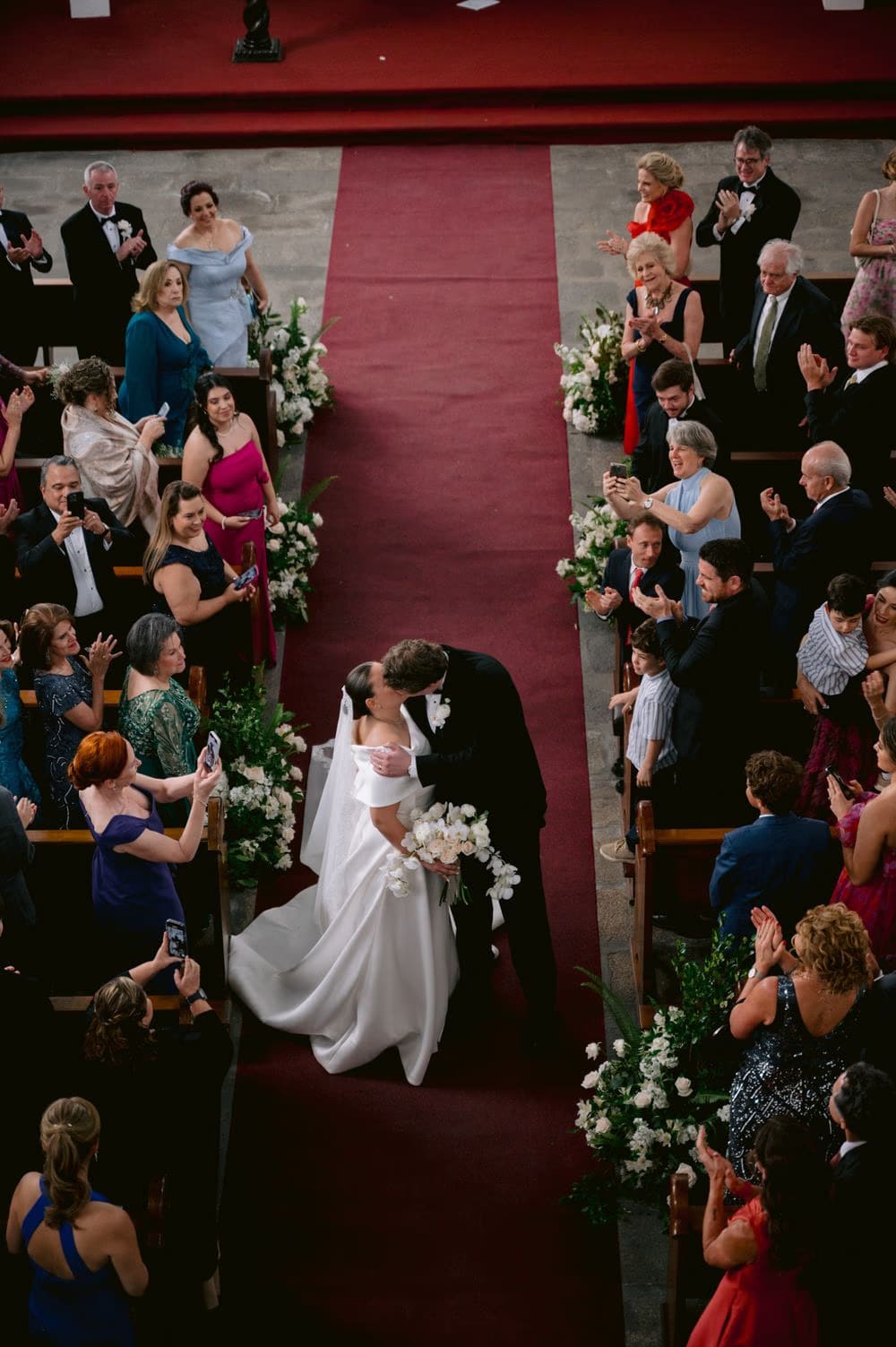 Aerial view of the couple's first kiss in the aisle as guests celebrate around them.