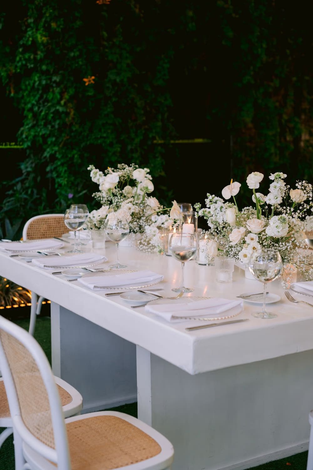 Reception table styled with white anthuriums, ranunculus and baby's breath in candlelight — florals by Decor Guatemala.