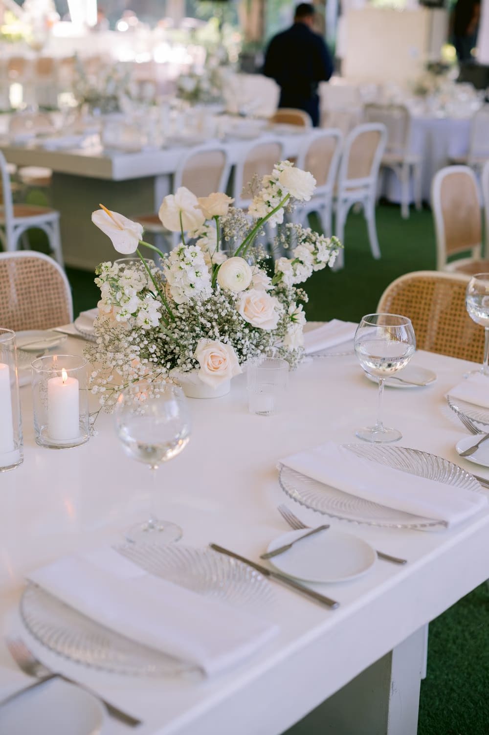 Modern white floral centerpiece with anthuriums and ranunculus on a long reception table — Decor Guatemala styling.