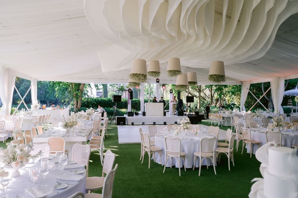 Open-air reception tent with draped fabric ceiling and baby's breath chandeliers set up on the lawn.