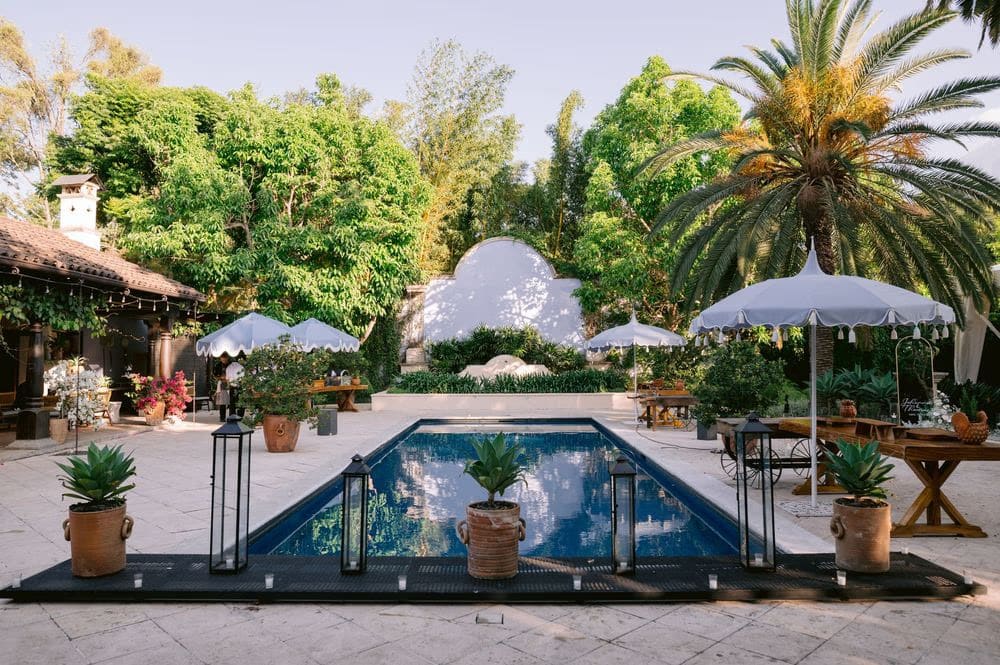 The signature infinity pool at Villa Bokeh framed by palms, parasol umbrellas and potted agaves — modern poolside wedding venue.