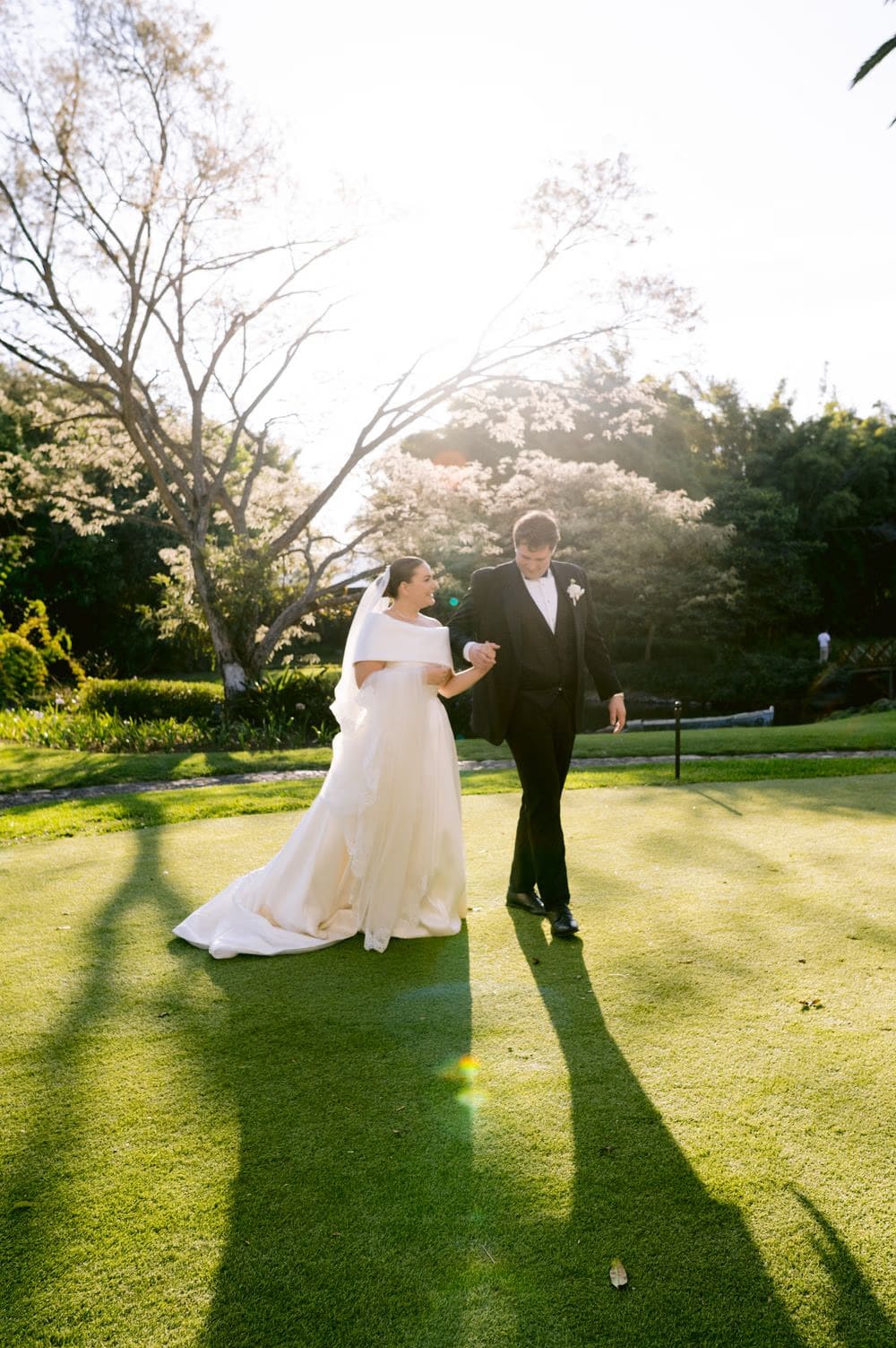 Sun-flared portrait of the newlyweds walking hand-in-hand across the lawn at Villa Bokeh.