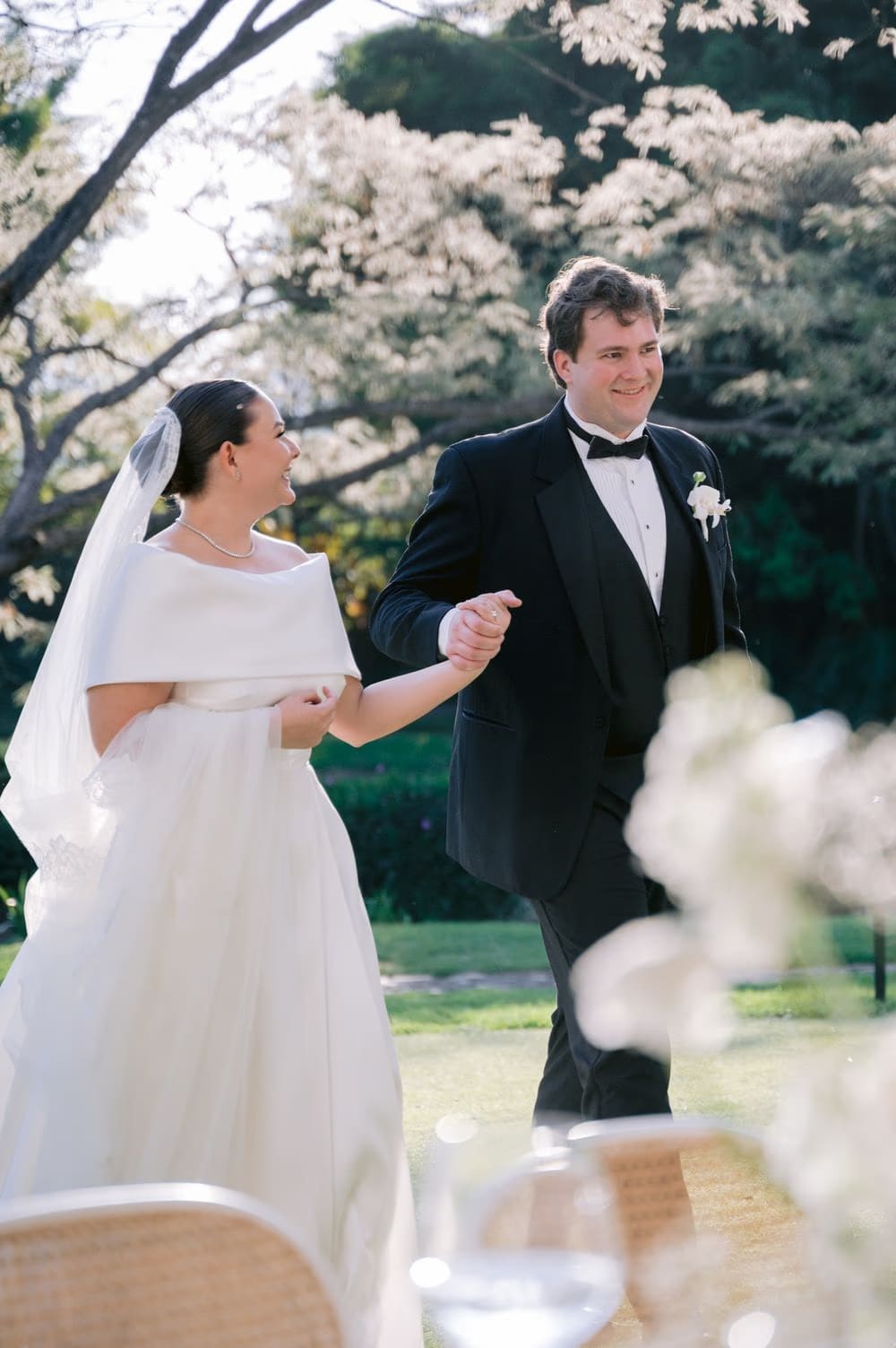 Newlyweds enter the open-air reception holding hands as guests look on — golden hour at Villa Bokeh.