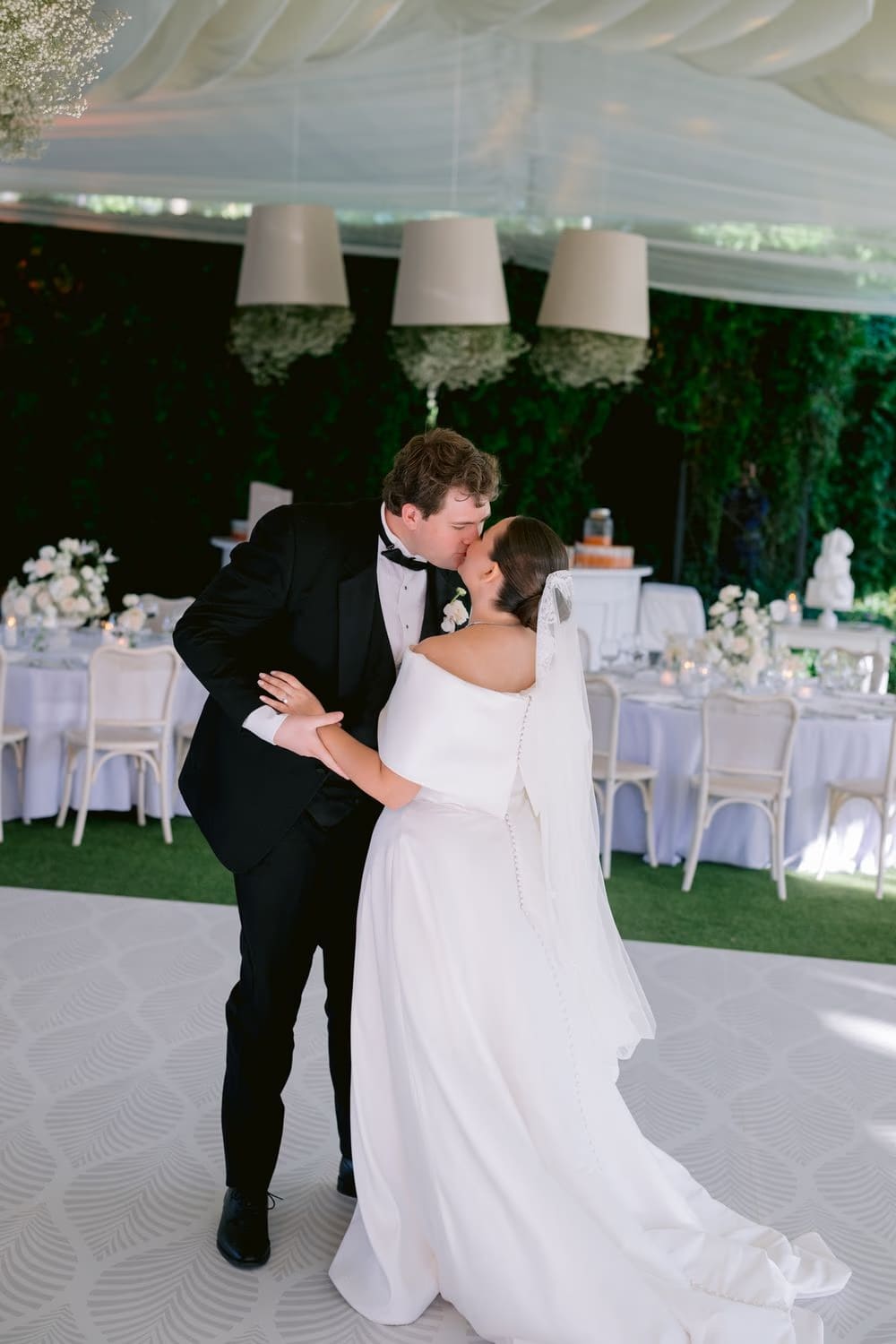 Bride and groom share a kiss mid-first-dance under draped fabric chandeliers at the reception.