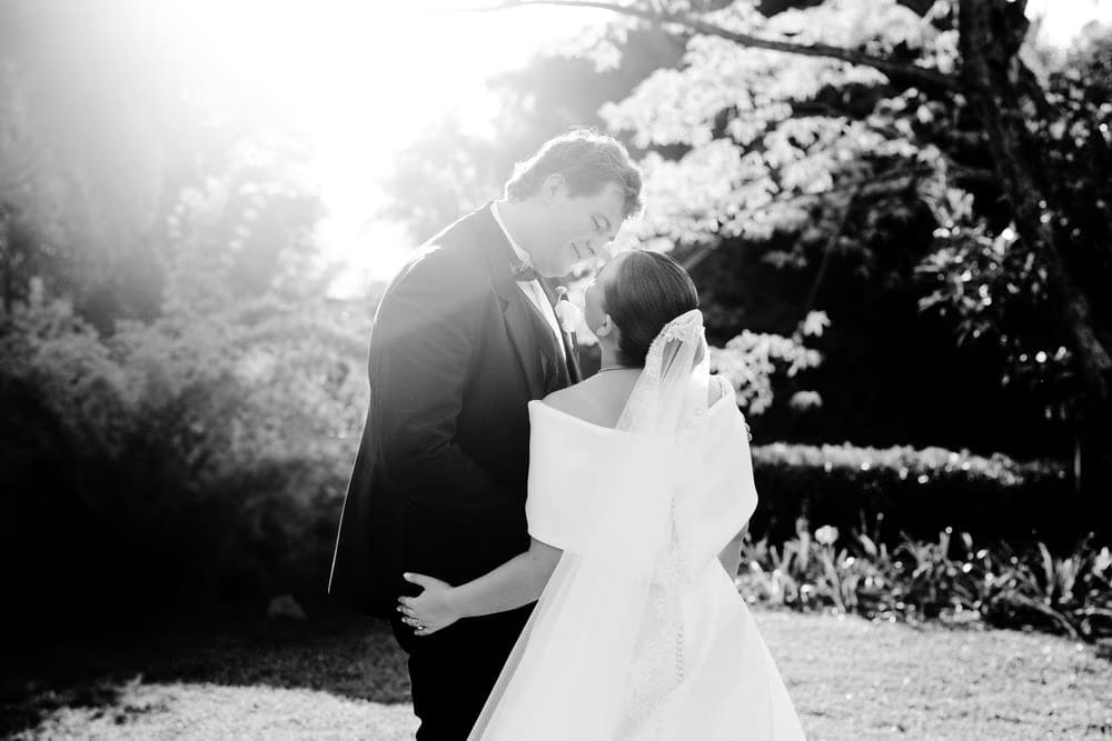Backlit black-and-white portrait of the couple about to kiss in the garden at golden hour.