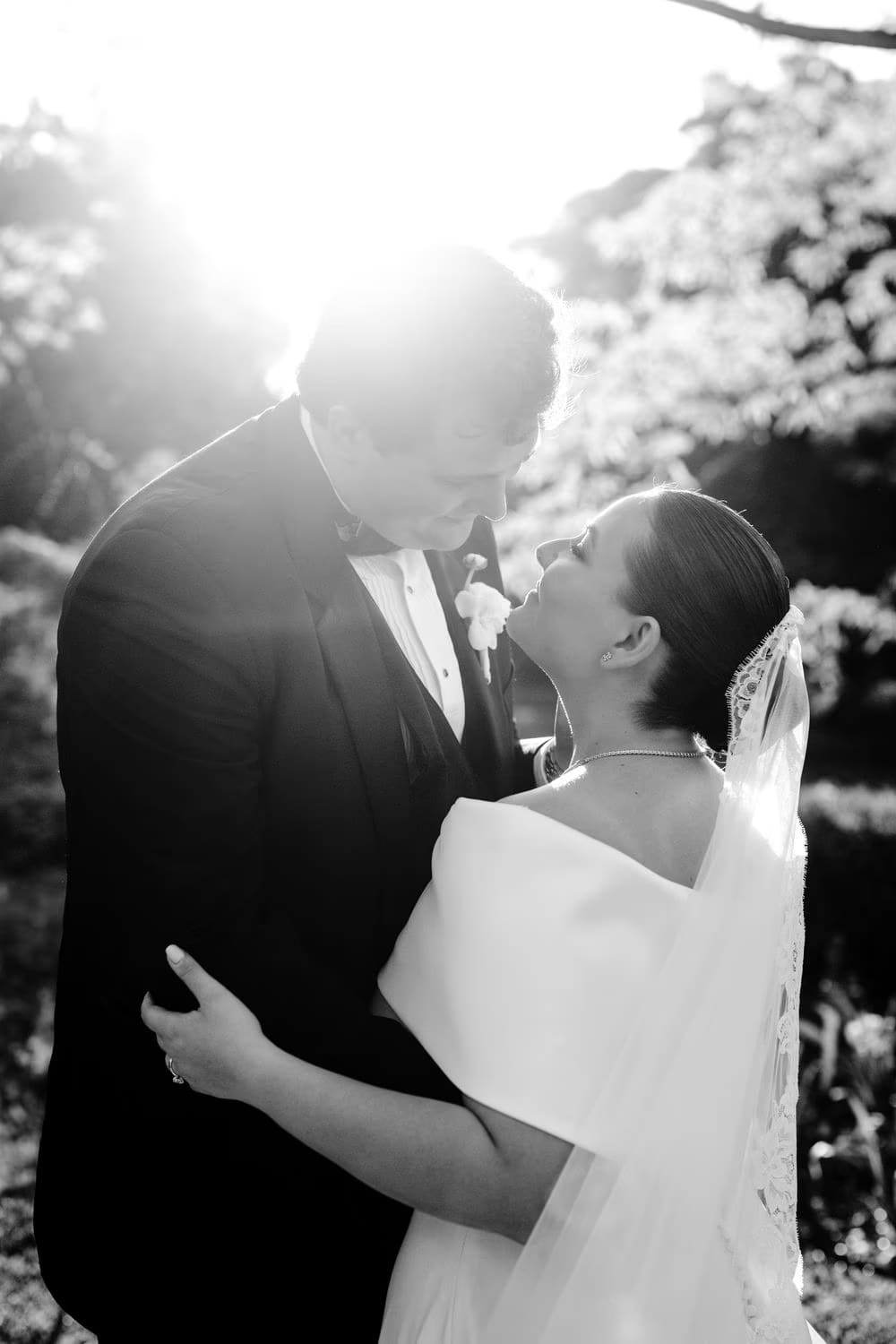 Black-and-white portrait of the couple laughing forehead-to-forehead with the sun flaring behind them.