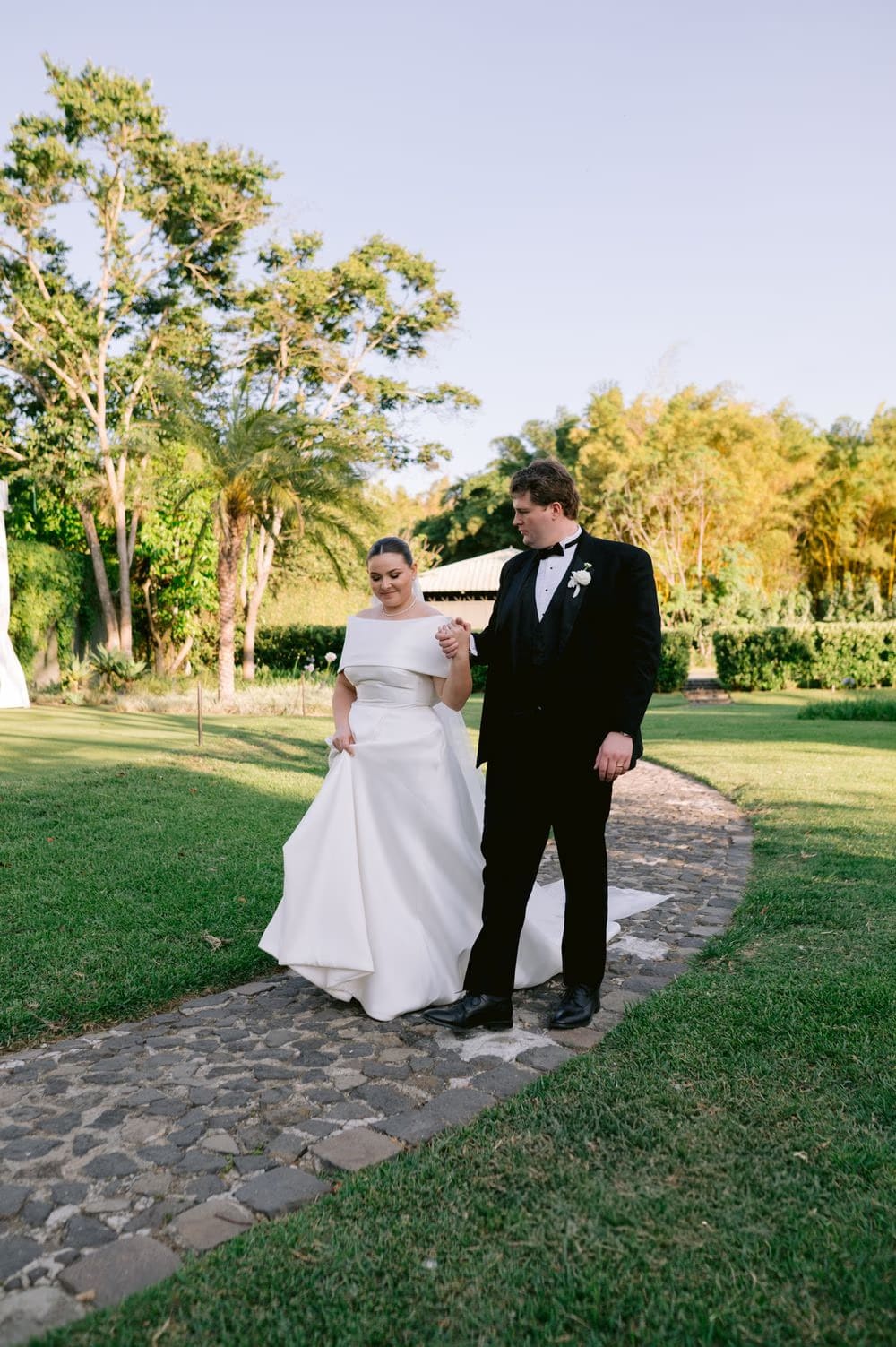 Bride and groom walk down a stone path on the grounds at sunset — destination wedding portrait.