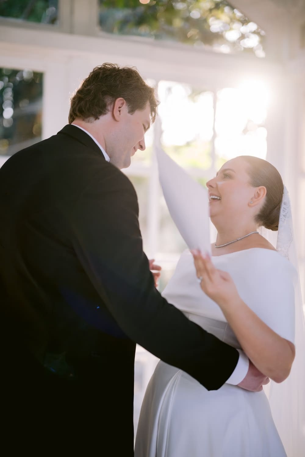 The couple laughs together while reading their private vows in the gazebo.