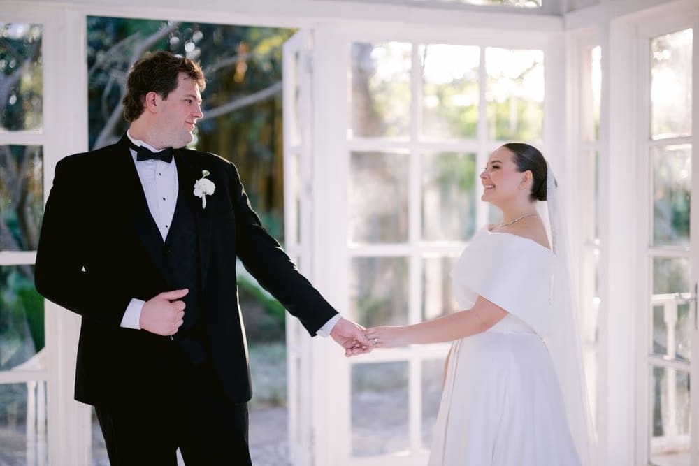 Bride and groom hold hands inside the open-air gazebo, the bride's veil glowing in backlight.