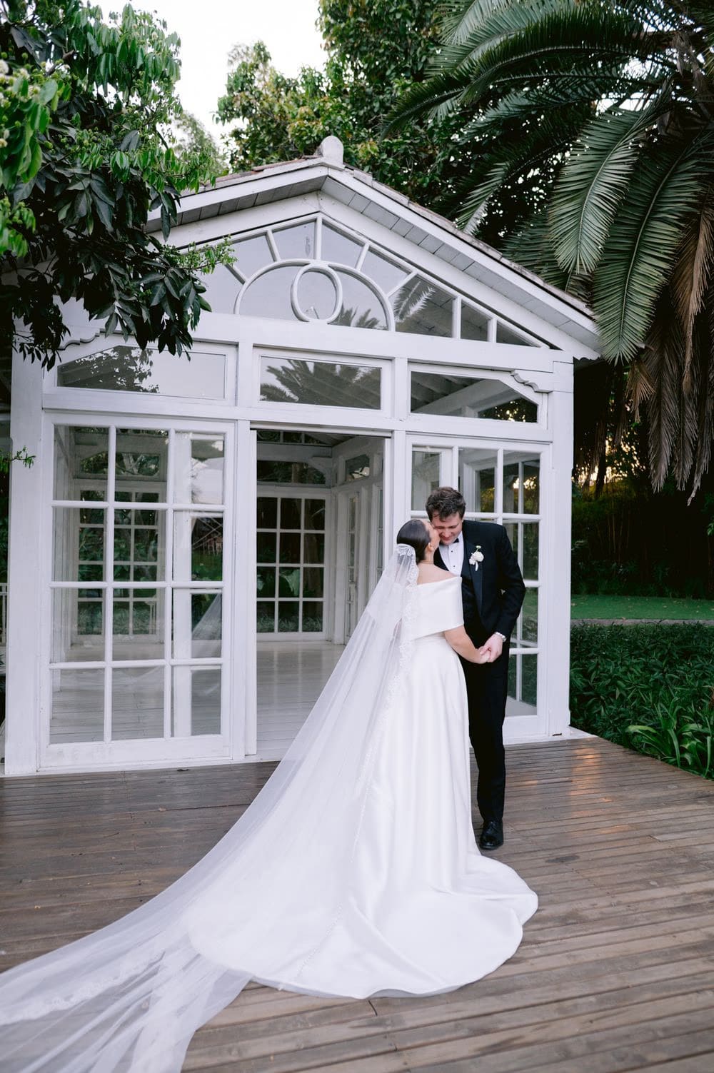 Bride and groom share a quiet embrace on the wooden deck outside the garden gazebo.