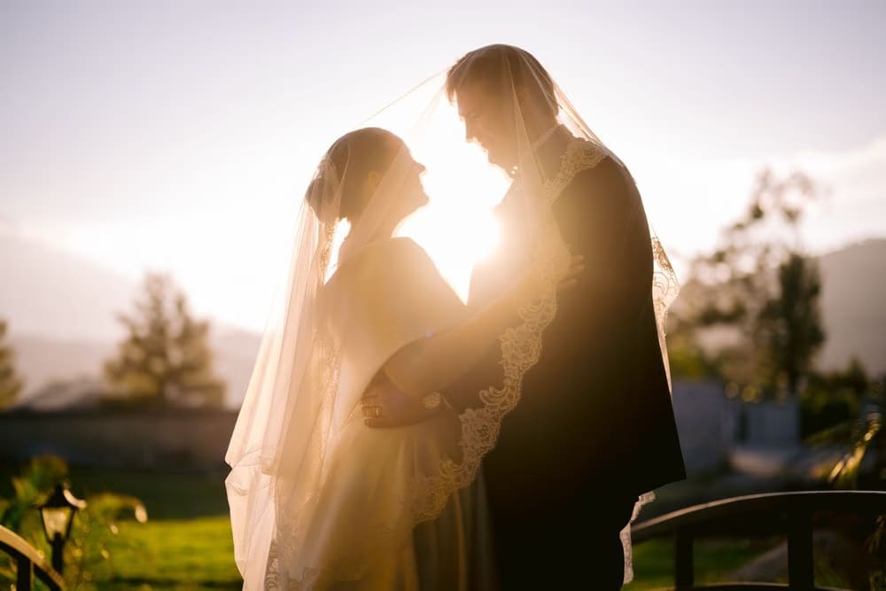 Couple framed by the cathedral veil with the sun blazing between them at golden hour — silhouette wedding portrait.