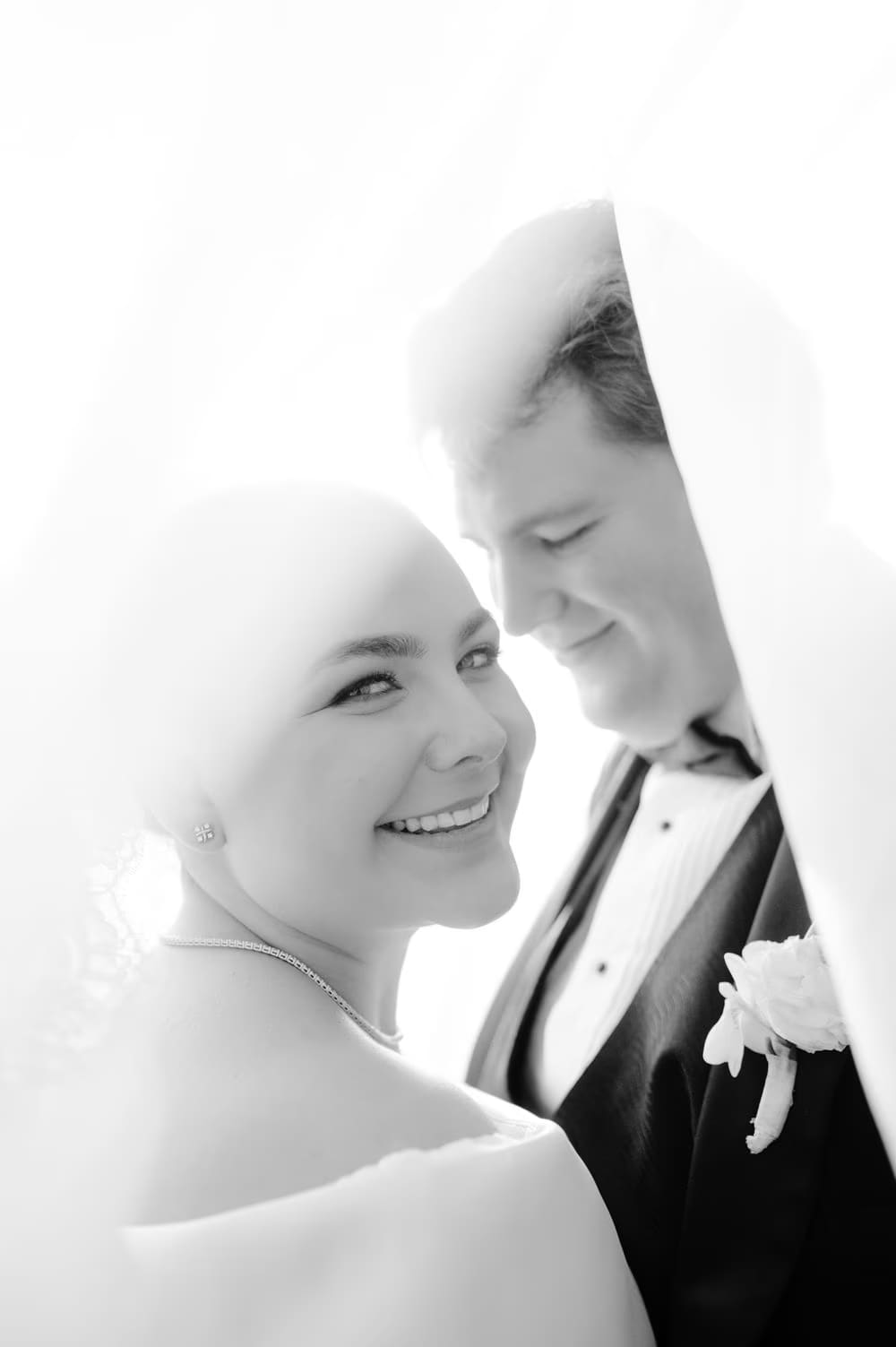 Black-and-white close-up of Johanna smiling beside Thomas, framed under the veil — editorial wedding portrait.