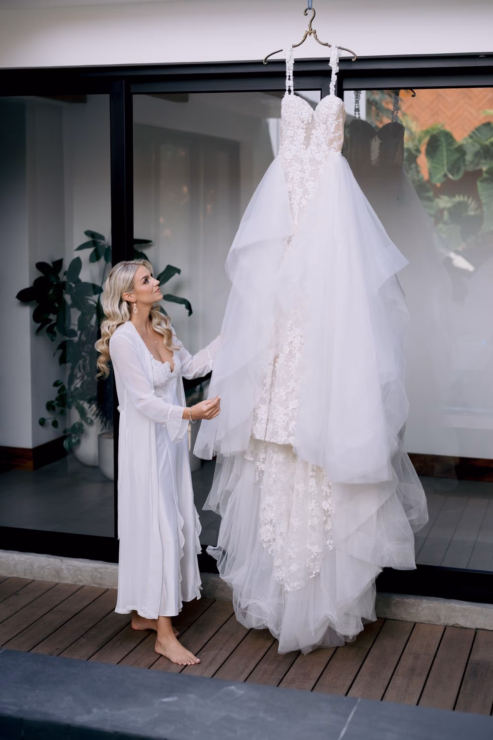 Bride in white robe gazes at her lace gown hanging in the suite at Casa Kuxtal before her wedding in La Antigua.